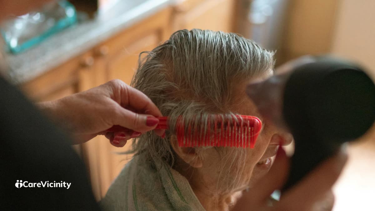 Woman helping an older woman with her hair at a home bathroom mirror