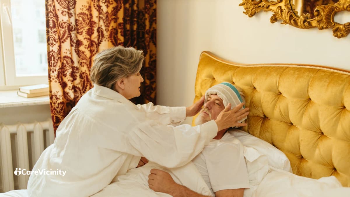 An older woman applying a cool, damp cloth to an older man's forehead while he rests in bed
