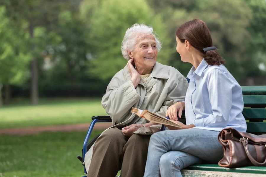 Older woman in wheelchair talking with another woman on park bench