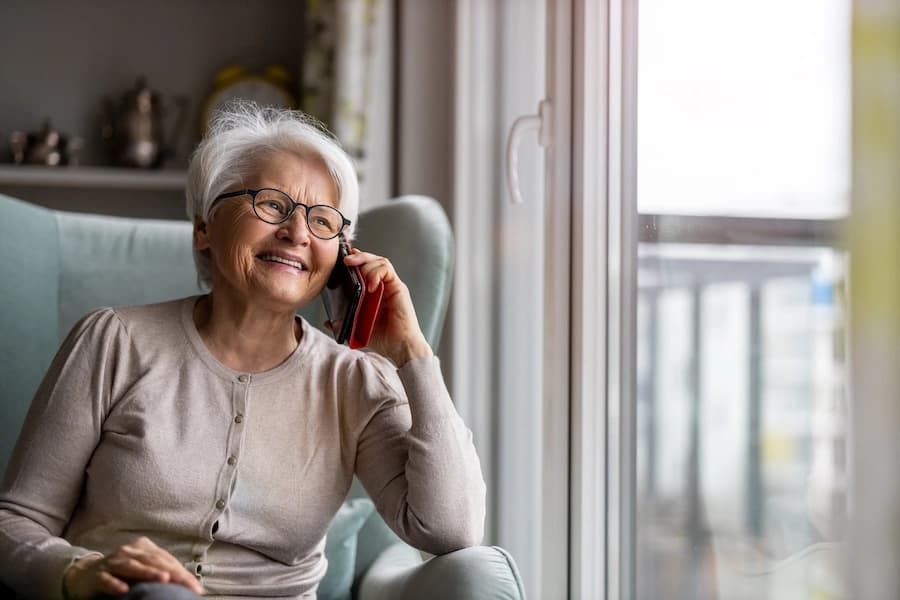 Older woman sitting in a chair talking on the phone by a window