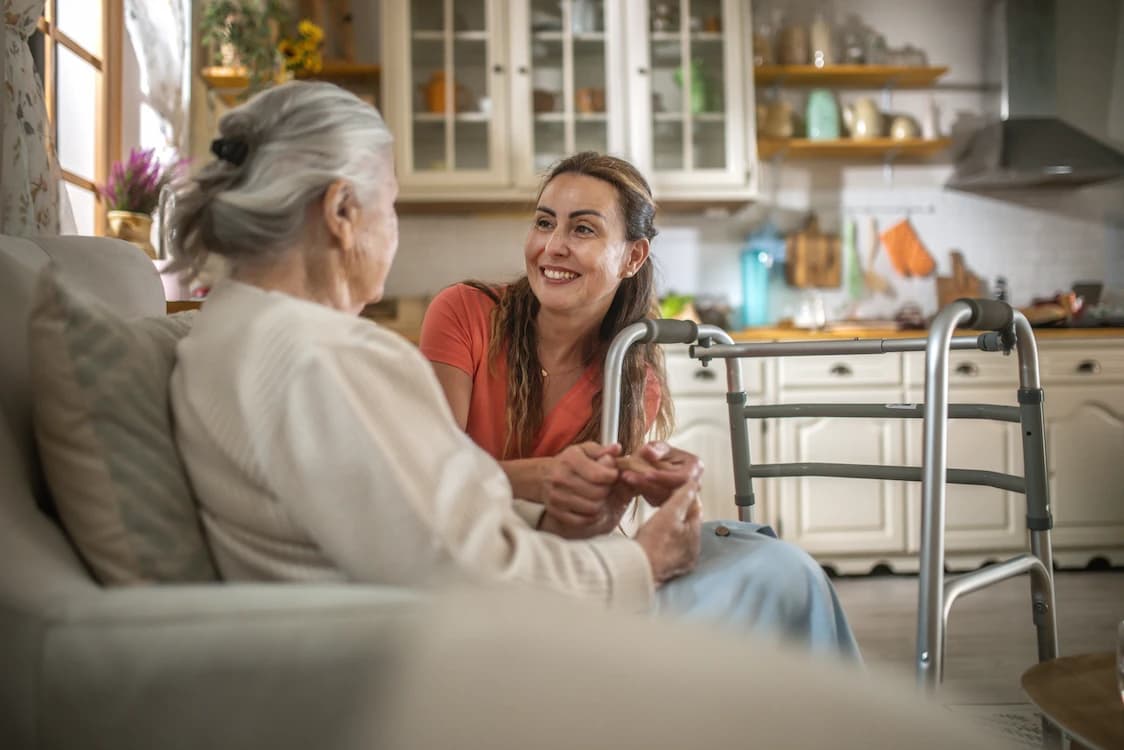 Support worker smiling with an older woman at home beside her walking frame