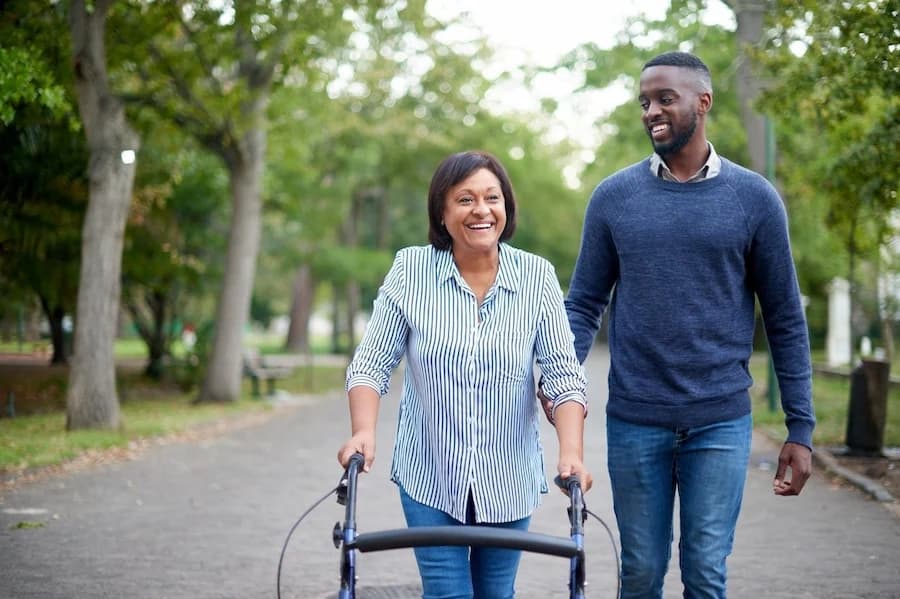 Woman using a walking frame while walking outdoors with another man