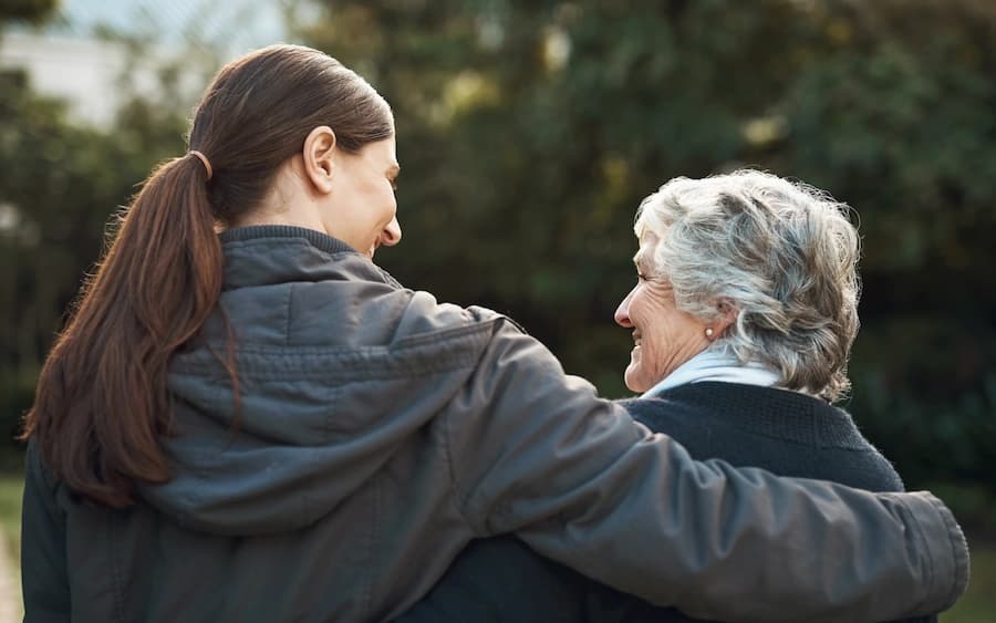 Younger woman with arm around an older woman while walking outdoors