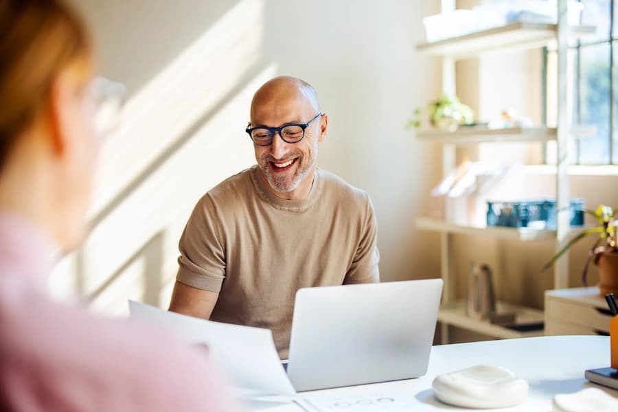 Man sitting at a desk smiling while using a laptop