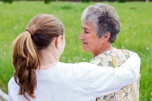 Younger woman with arm around older woman while standing outdoors