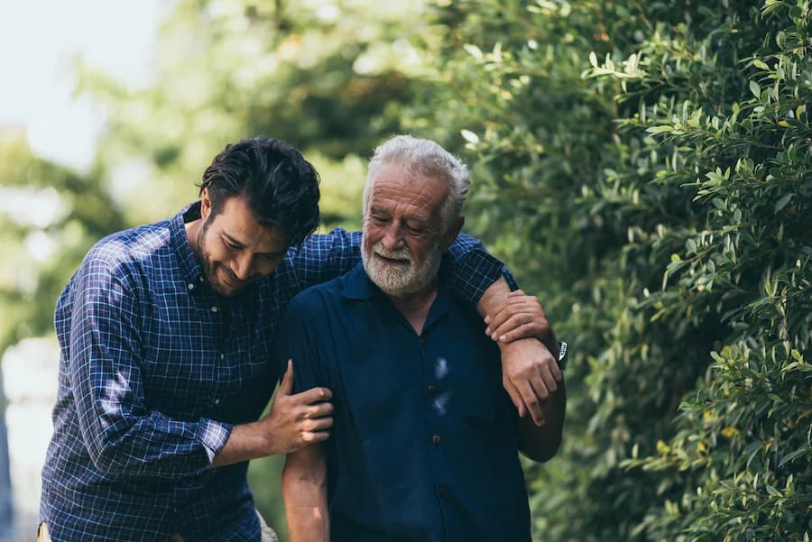 Adult son walking beside his elderly father and offering support outdoors