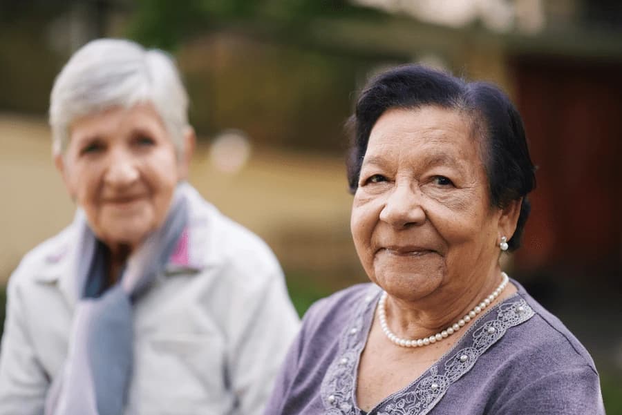 Two older women sitting outdoors and looking at the camera