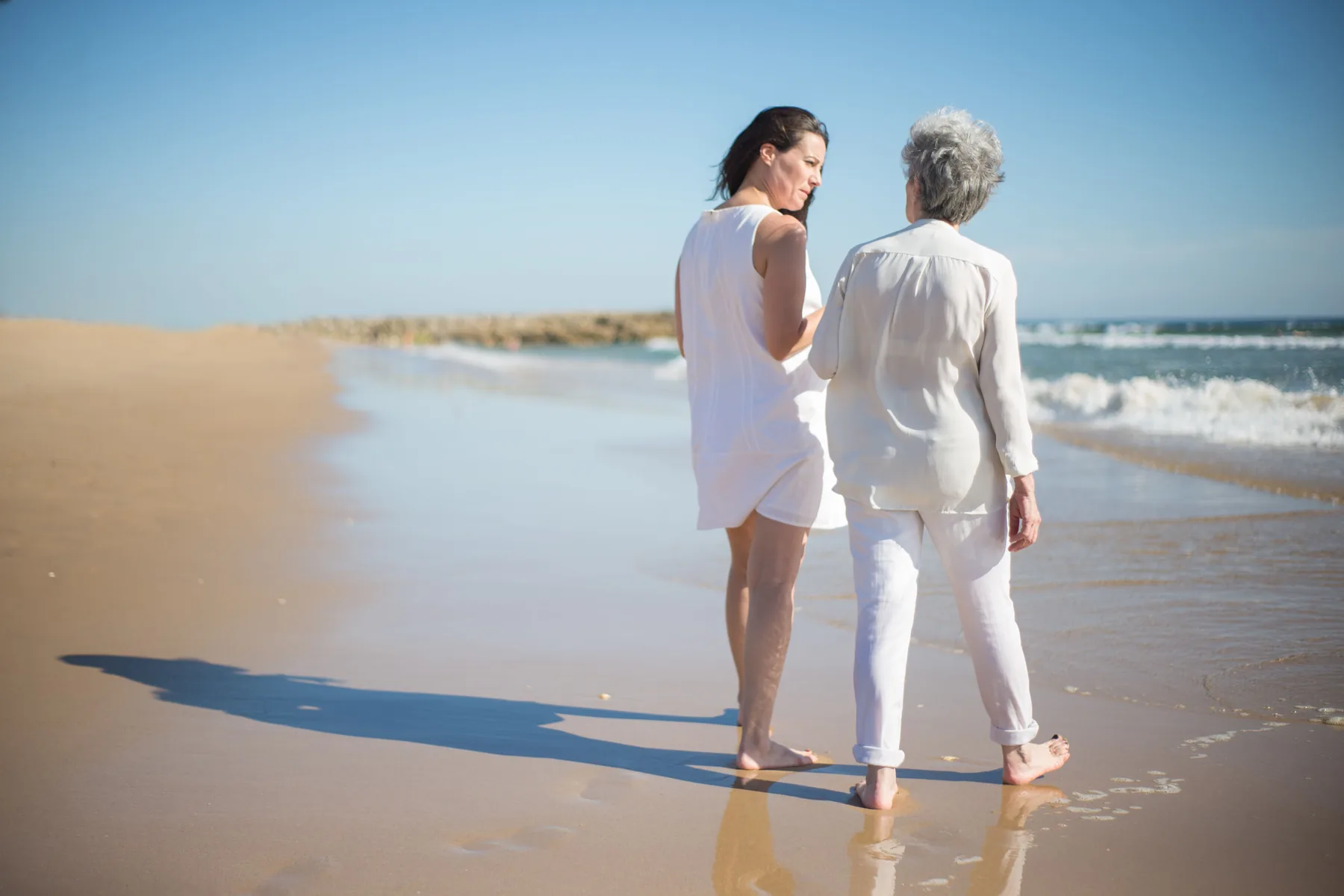 Older woman and a younger woman walking together along the beach