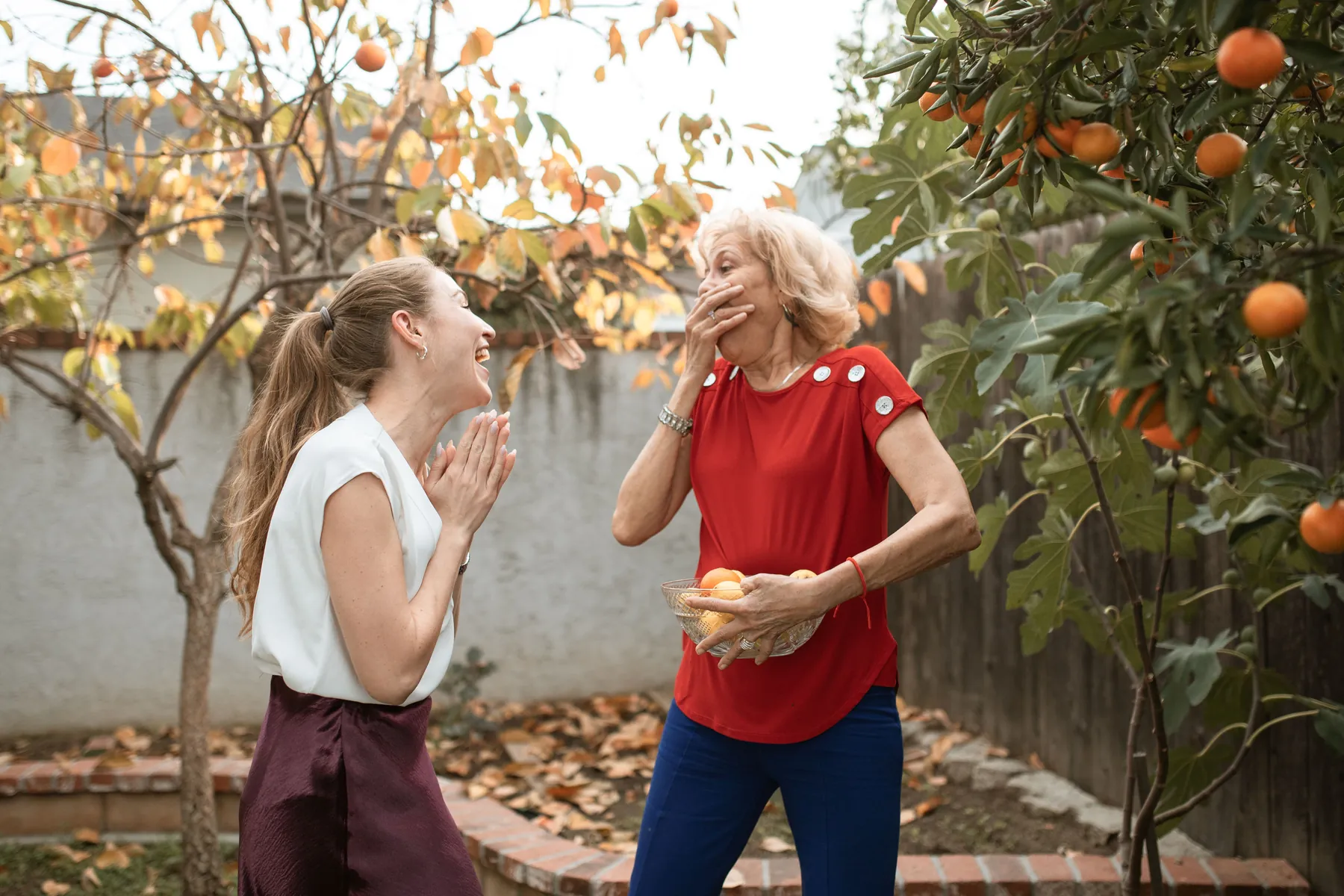 Older woman and a younger woman laughing together in a backyard garden