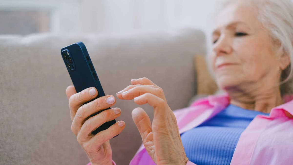 An older woman sitting on a sofa at home reading a message on her phone