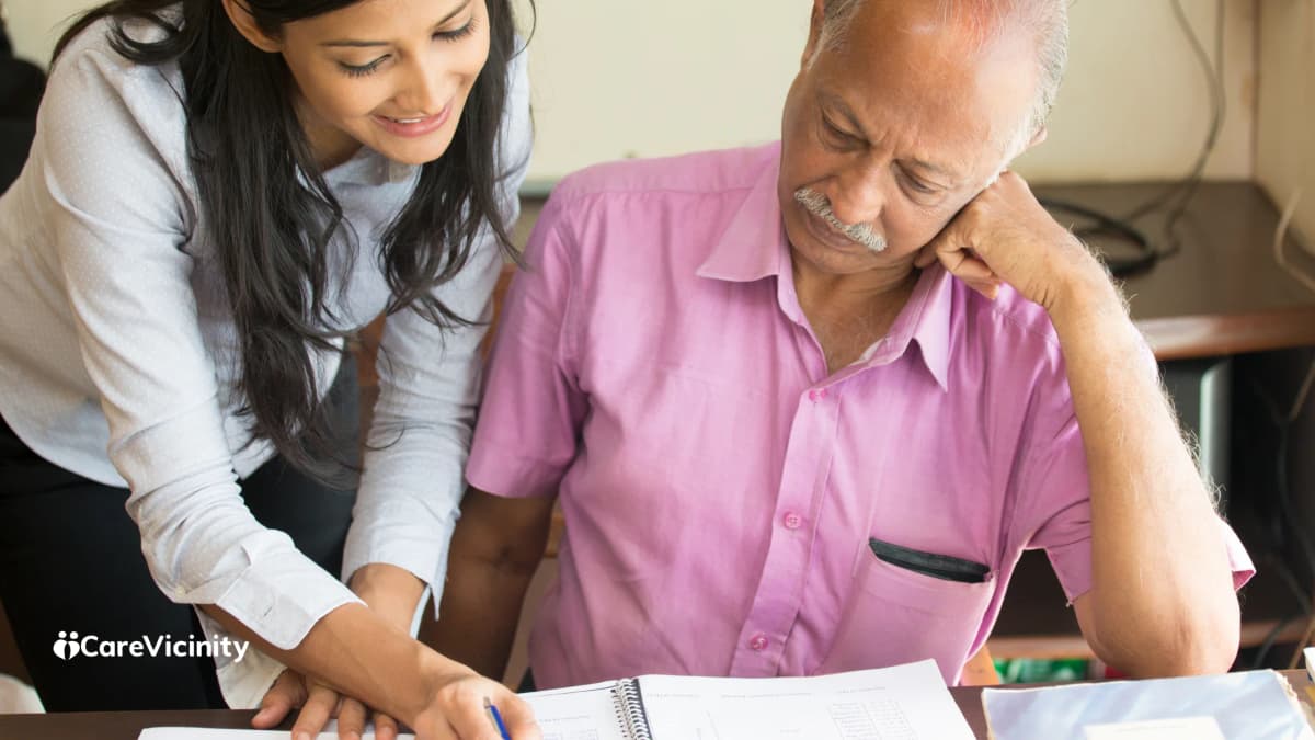 A support worker leaning in to talk with an older man as they look through papers together