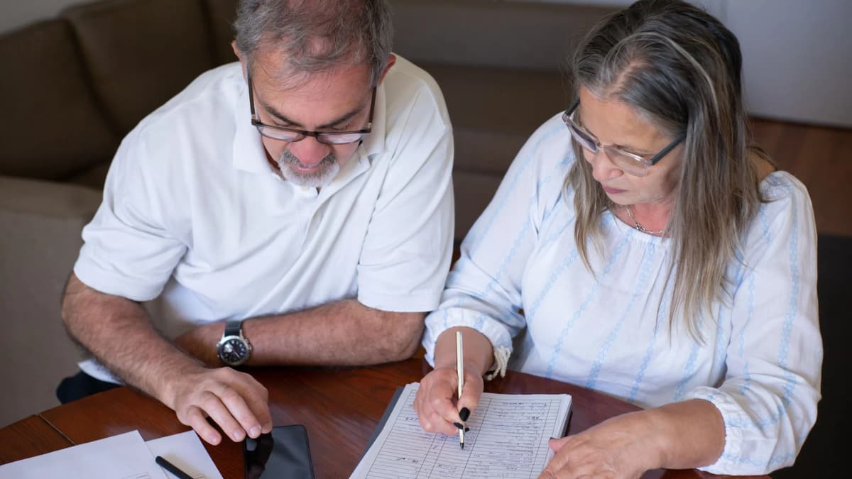 An older man and woman at a table at home going through a written form together
