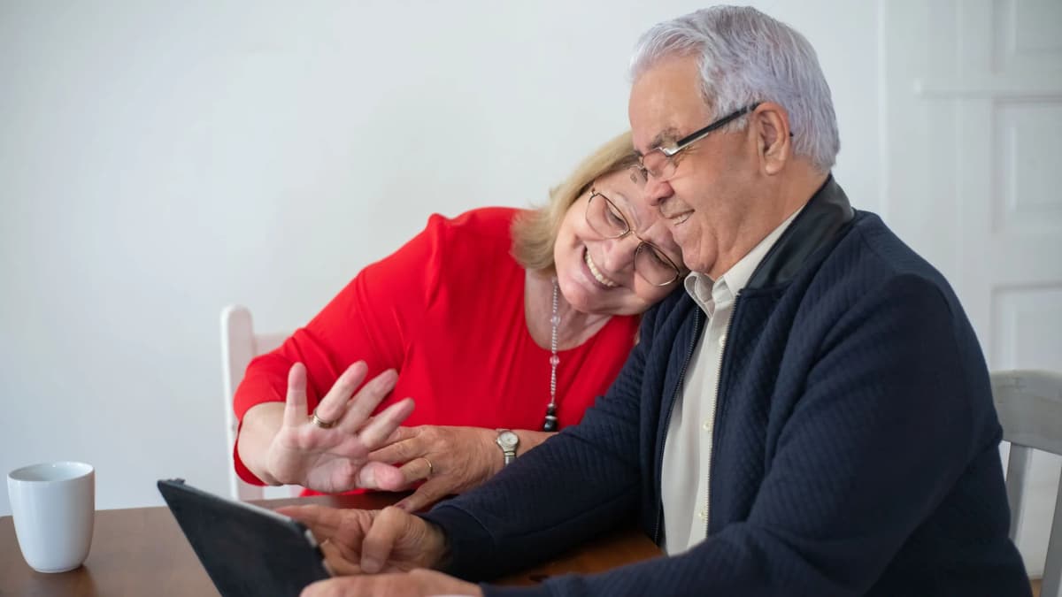 Older couple smiling together at a tablet on a kitchen table at home