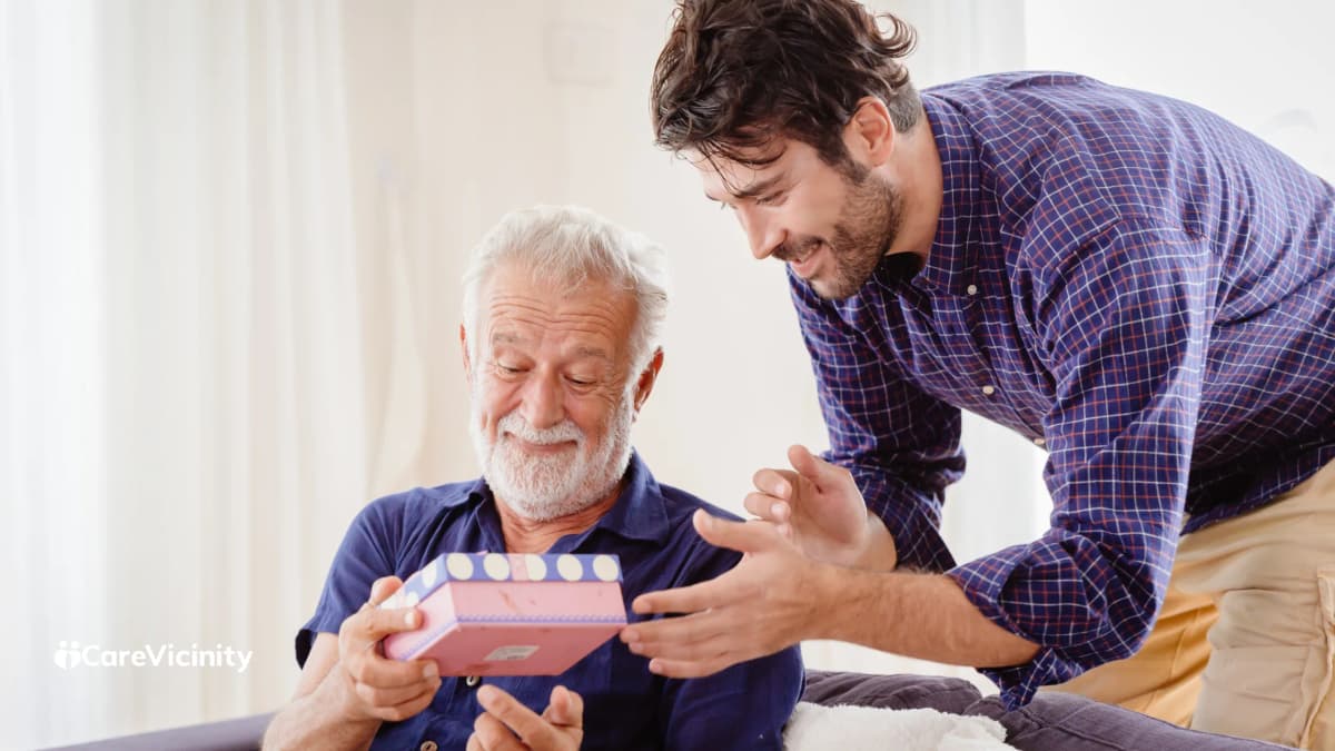 Older man smiling as a younger man hands him a gift box at home
